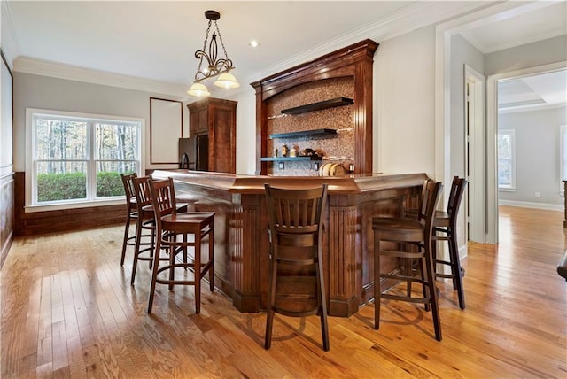 bar with light hardwood / wood-style floors, black fridge, ornamental molding, and hanging light fixtures