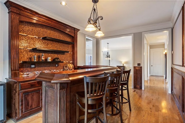 bar featuring dark brown cabinetry, crown molding, and hanging light fixtures