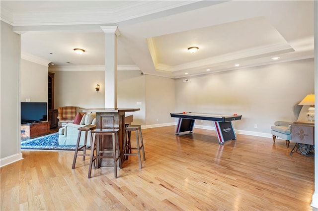 rec room with light wood-type flooring, a tray ceiling, bar, and ornamental molding