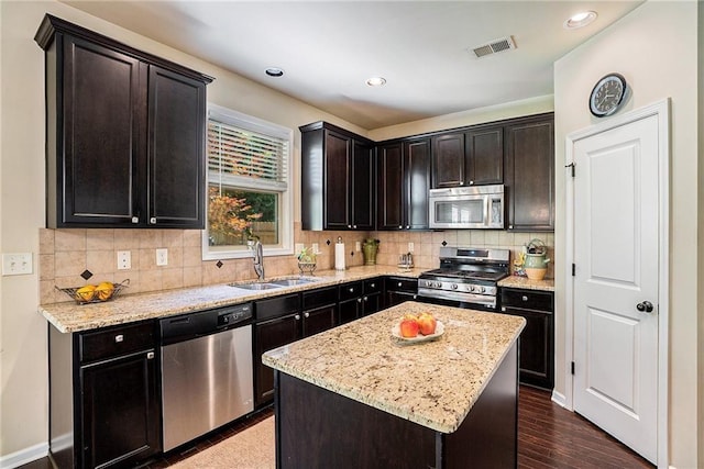 kitchen with appliances with stainless steel finishes, sink, a center island, dark brown cabinetry, and light stone counters