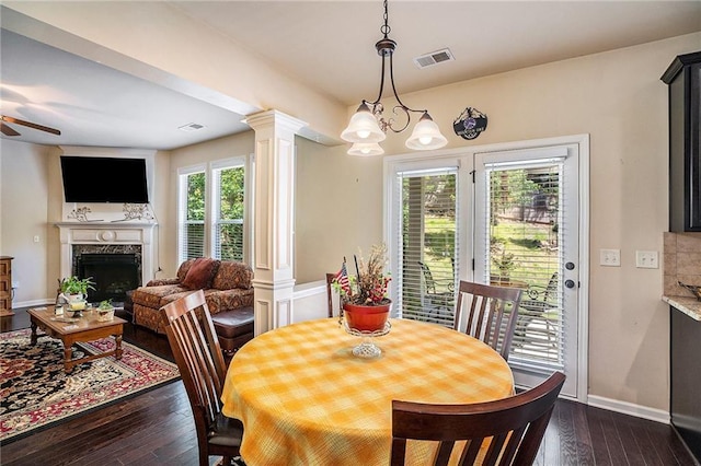 dining area featuring ornate columns, dark wood-type flooring, ceiling fan with notable chandelier, and a high end fireplace