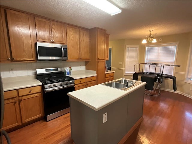 kitchen with dark wood-type flooring, hanging light fixtures, an island with sink, stainless steel appliances, and a chandelier