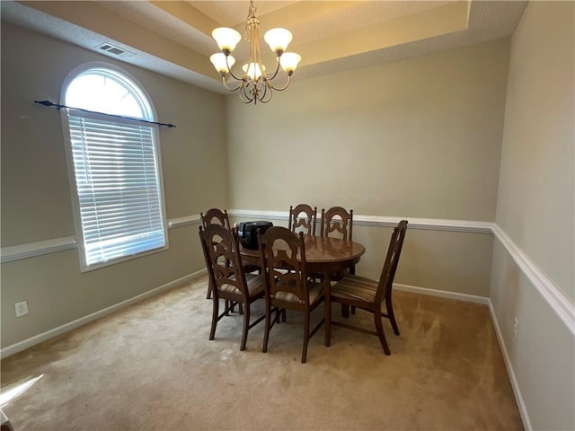 carpeted dining area with a notable chandelier and a tray ceiling