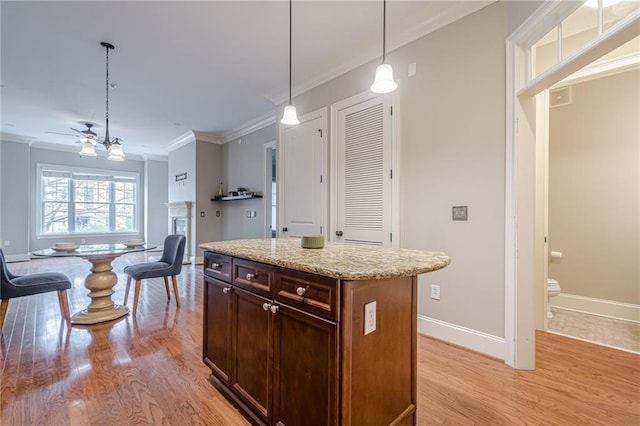 kitchen featuring light stone counters, hanging light fixtures, light wood-type flooring, ornamental molding, and a kitchen island