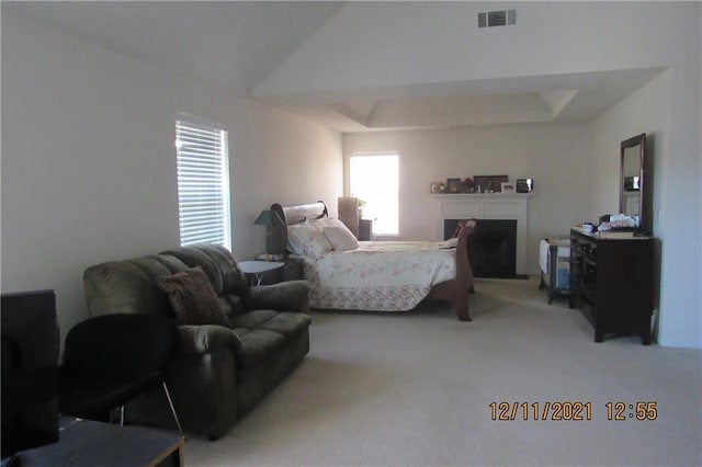 bedroom with carpet floors, lofted ceiling, a raised ceiling, visible vents, and a fireplace with raised hearth