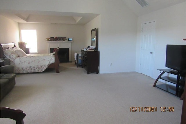 carpeted bedroom featuring visible vents, a fireplace with raised hearth, and a raised ceiling