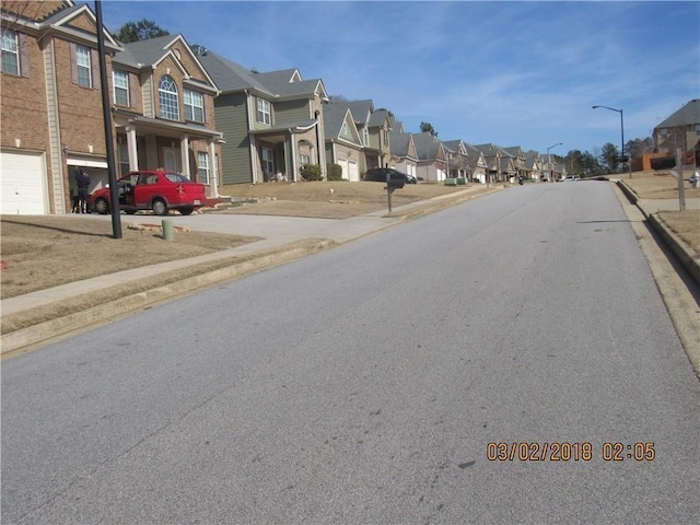 view of street featuring street lights, curbs, sidewalks, and a residential view