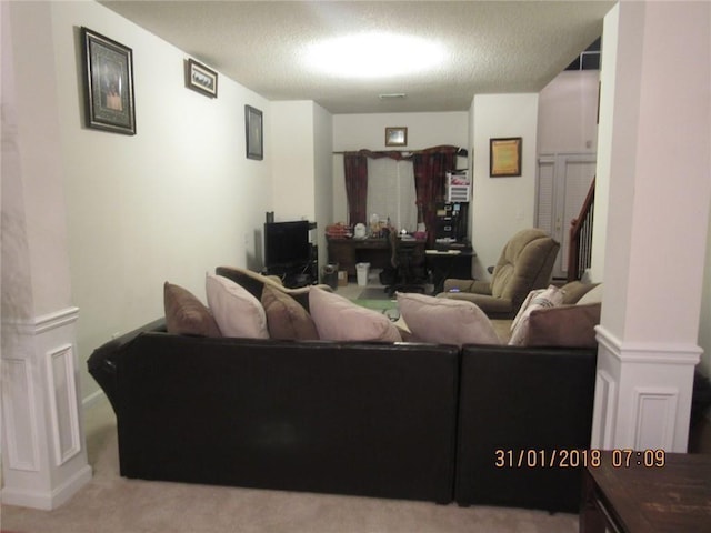 carpeted living area with a textured ceiling and ornate columns