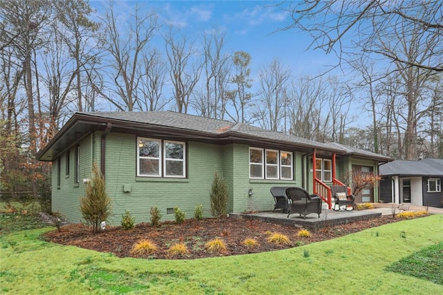 view of front facade with a shingled roof, a patio, crawl space, a front lawn, and brick siding