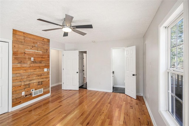 unfurnished bedroom featuring a textured ceiling, light wood-style flooring, a ceiling fan, visible vents, and baseboards