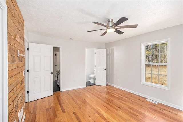 unfurnished bedroom featuring a textured ceiling, connected bathroom, visible vents, baseboards, and light wood finished floors