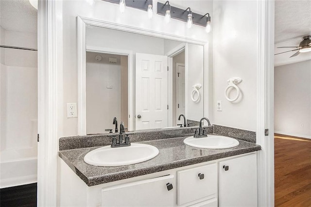 full bath with double vanity, ceiling fan, a sink, and wood finished floors