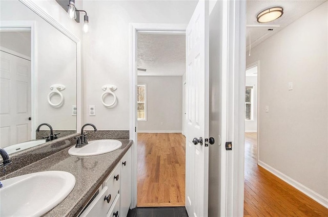 bathroom with double vanity, a sink, a textured ceiling, and wood finished floors