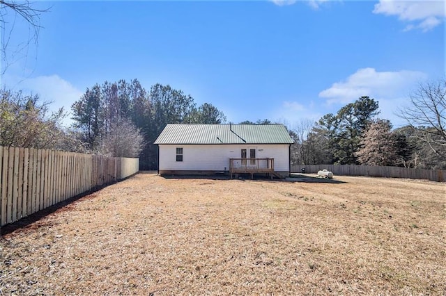 back of property with a fenced backyard, metal roof, and a wooden deck