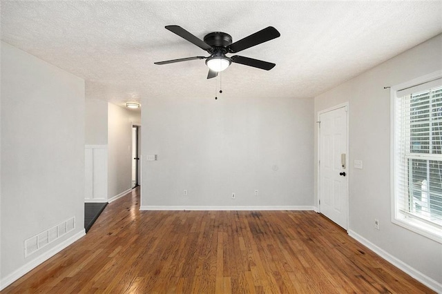 empty room with a textured ceiling, visible vents, a wealth of natural light, and wood finished floors