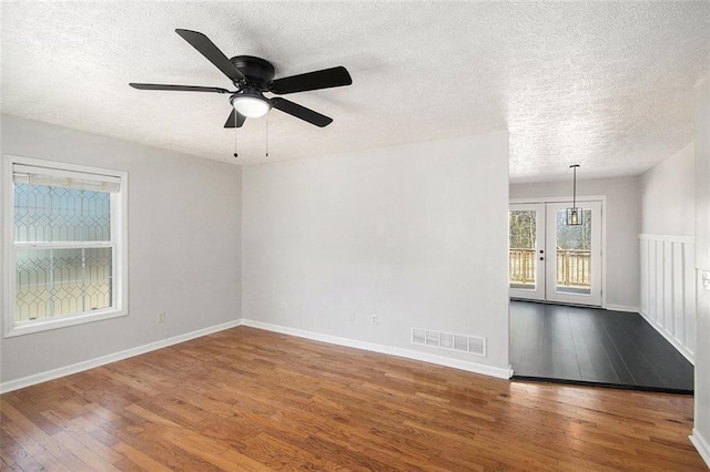 spare room featuring wood-type flooring, visible vents, a textured ceiling, and baseboards