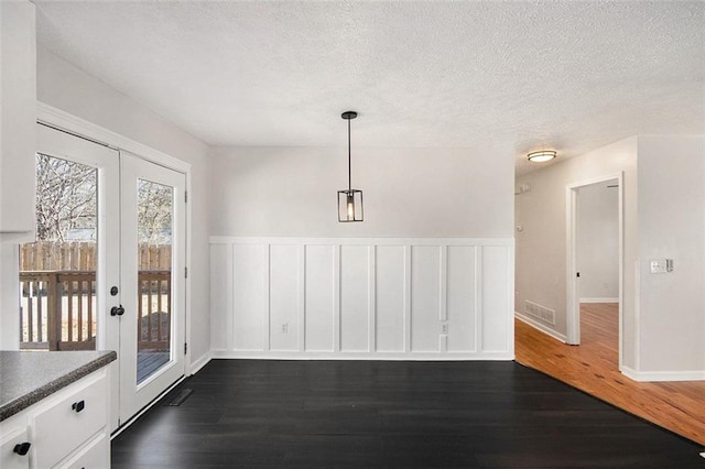 unfurnished dining area with french doors, visible vents, a textured ceiling, and dark wood-style flooring