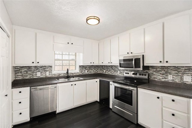 kitchen with dark wood finished floors, white cabinets, dark countertops, appliances with stainless steel finishes, and a sink