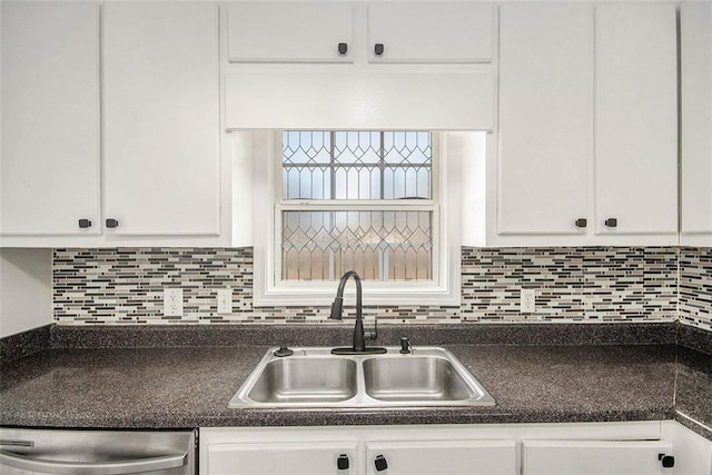 kitchen with stainless steel dishwasher, dark countertops, a sink, and white cabinetry