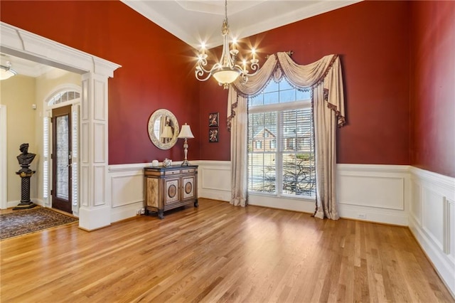 unfurnished dining area featuring a chandelier, a wainscoted wall, light wood-style floors, and a decorative wall