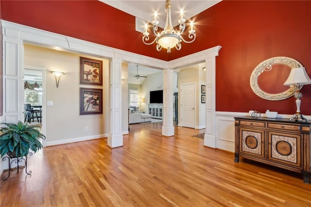 dining space with a decorative wall, light wood finished floors, ornate columns, and ceiling fan with notable chandelier