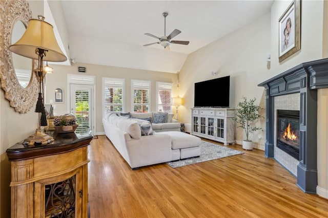 living room with ceiling fan, a fireplace, baseboards, vaulted ceiling, and light wood finished floors