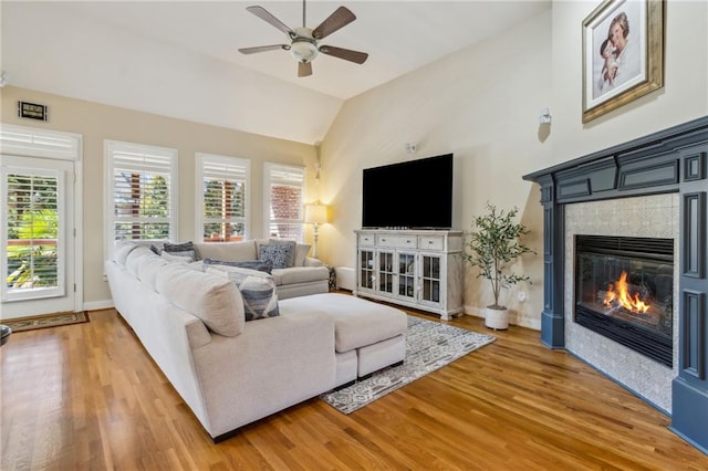 living area with a fireplace, light wood-style floors, vaulted ceiling, ceiling fan, and baseboards