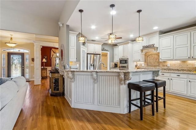 kitchen with decorative columns, a breakfast bar area, stainless steel appliances, backsplash, and light wood-style floors