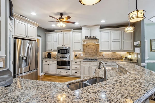 kitchen featuring tasteful backsplash, appliances with stainless steel finishes, light stone counters, decorative light fixtures, and a sink