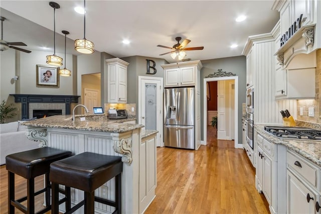 kitchen with light wood-style flooring, appliances with stainless steel finishes, a breakfast bar, open floor plan, and a fireplace