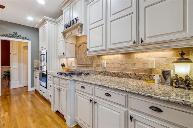 kitchen with stainless steel appliances, tasteful backsplash, light stone countertops, and light wood-style floors