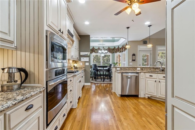 kitchen with a ceiling fan, decorative light fixtures, stainless steel appliances, light wood-type flooring, and a sink