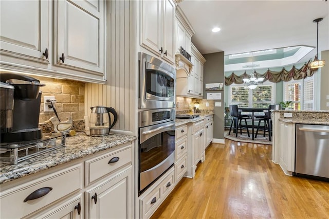 kitchen with light wood finished floors, appliances with stainless steel finishes, hanging light fixtures, a chandelier, and backsplash