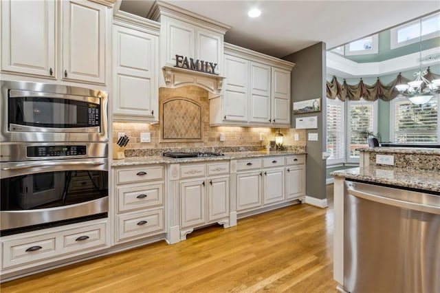 kitchen with light wood finished floors, a notable chandelier, stainless steel appliances, and backsplash