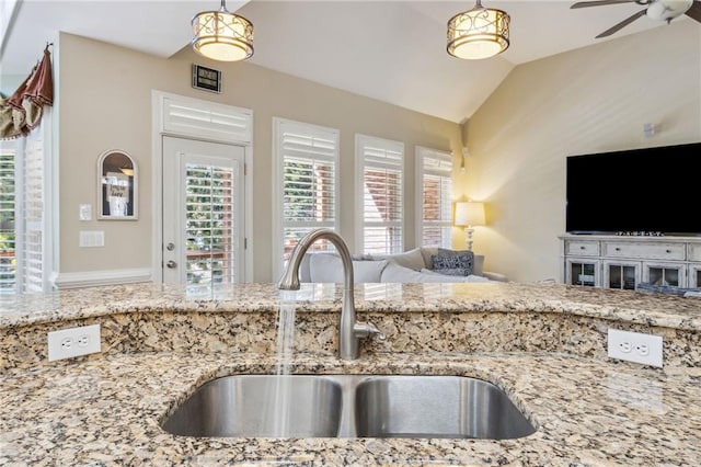 kitchen featuring vaulted ceiling, light stone counters, open floor plan, and a sink