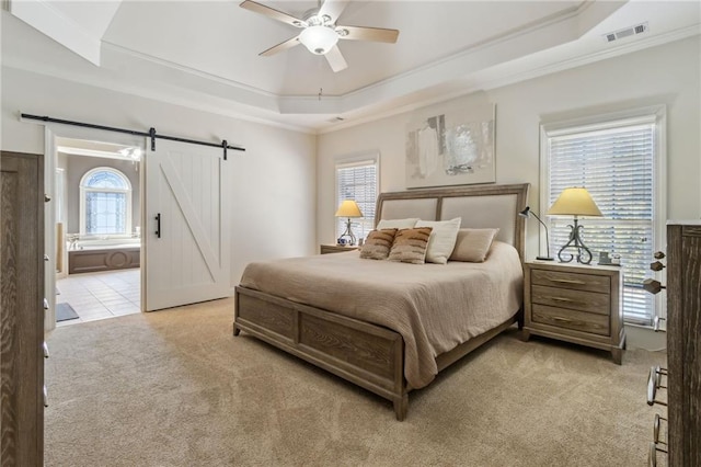 bedroom featuring a barn door, multiple windows, a tray ceiling, and light colored carpet