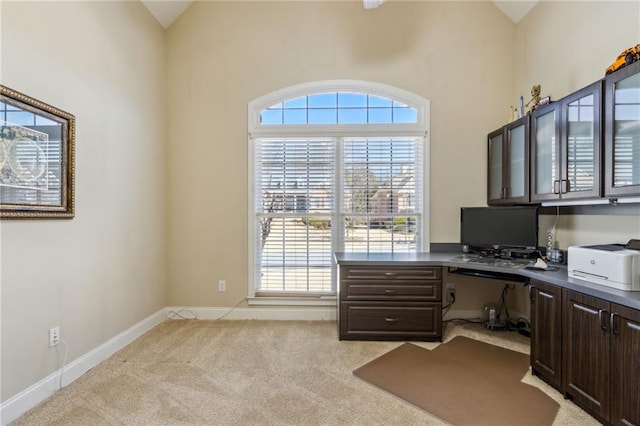 office space with baseboards, built in desk, and light colored carpet