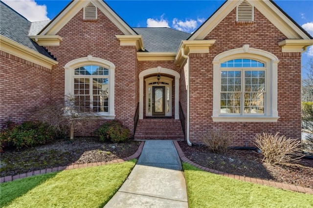 doorway to property featuring a shingled roof and brick siding