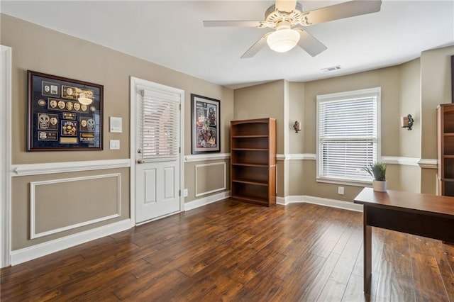 unfurnished office with dark wood-style floors, visible vents, a decorative wall, and a ceiling fan