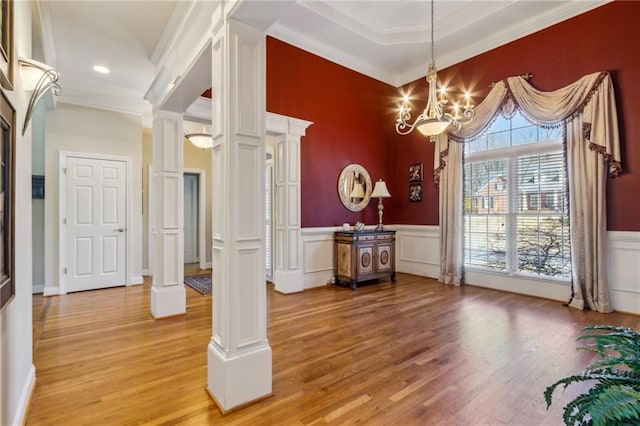 dining space featuring a notable chandelier, ornamental molding, wainscoting, light wood-type flooring, and ornate columns