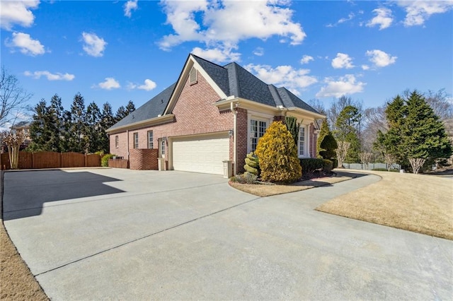 view of side of home with roof with shingles, brick siding, fence, a garage, and driveway