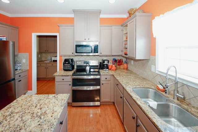 kitchen featuring crown molding, light wood finished floors, stainless steel appliances, tasteful backsplash, and a sink