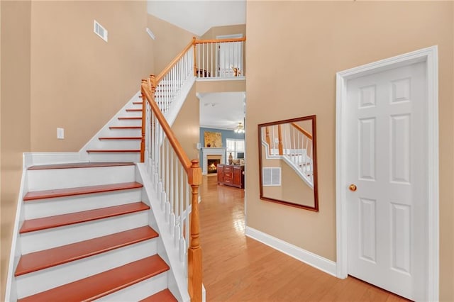 stairs with a lit fireplace, visible vents, baseboards, and wood finished floors