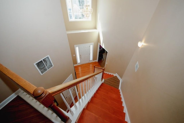 stairs with a towering ceiling, baseboards, visible vents, and wood finished floors