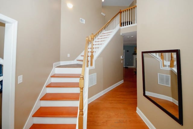 stairs featuring a towering ceiling, wood finished floors, visible vents, and baseboards