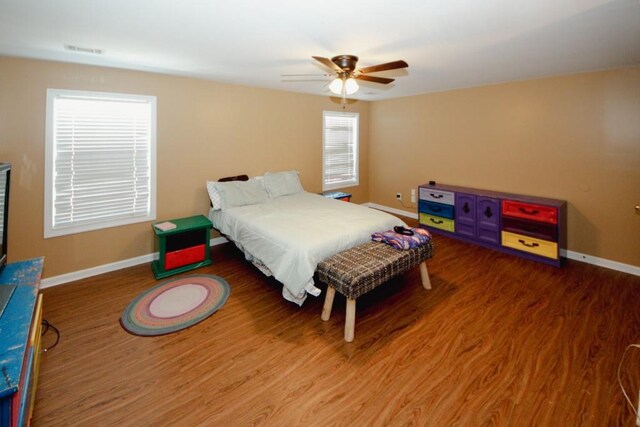 bedroom featuring a ceiling fan, visible vents, baseboards, and wood finished floors