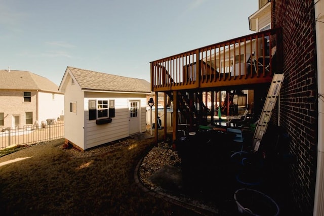 rear view of property featuring a wooden deck, fence, a shingled roof, and an outdoor structure