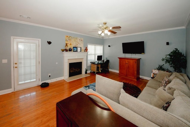 living area featuring light wood-style floors, baseboards, ornamental molding, and a fireplace with raised hearth