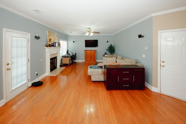 living room featuring light wood-type flooring, a glass covered fireplace, visible vents, and crown molding