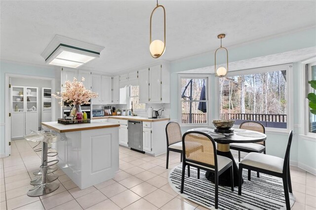 kitchen with light tile patterned floors, white cabinetry, a center island, dishwasher, and decorative light fixtures